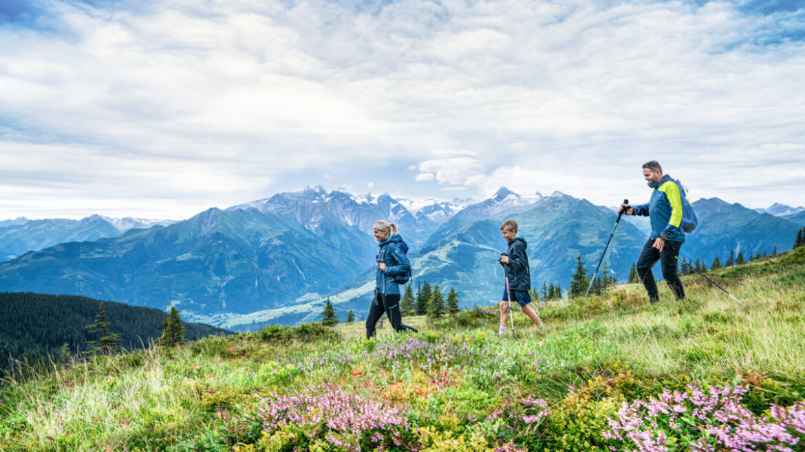 Man, woman and child hiking, flowers in front, mountains in backround