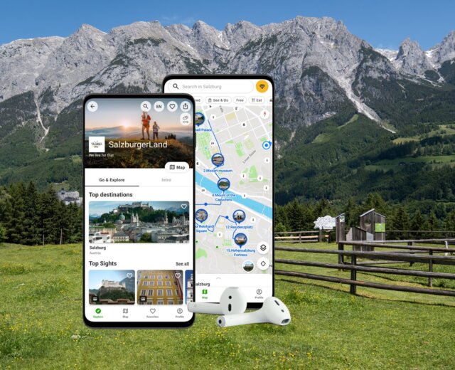 Two smartphones display a travel app; mountains, fields, and cows are in the background.