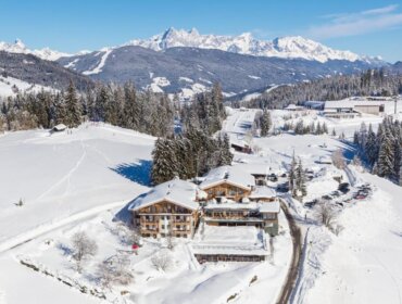 Aerial view of snowy mountain village with wooden lodges, pine trees, and Naturhotel Edelweiss Wagrain.