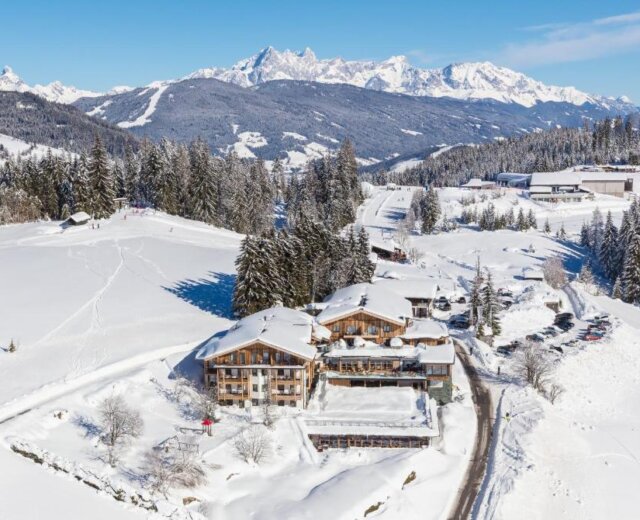 Aerial view of snowy mountain village with wooden lodges, pine trees, and Naturhotel Edelweiss Wagrain.