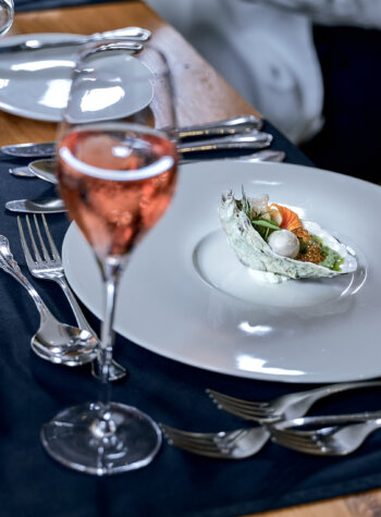 Elegant table setting with a plated gourmet starter and a glass of rosé wine on a wooden table.