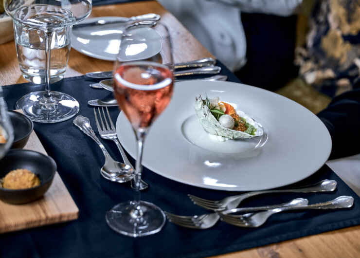 Elegant table setting with a plated gourmet starter and a glass of rosé wine on a wooden table.