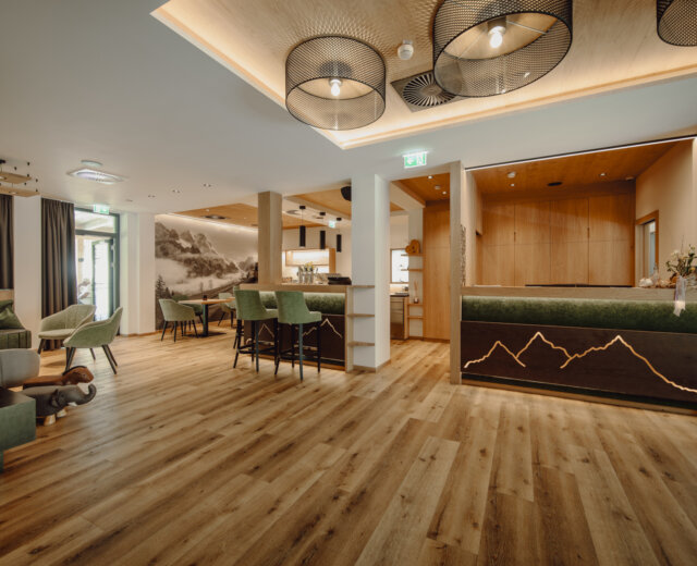 Modern hotel lobby with wooden floors, green seating, and a reception desk with mountain design.