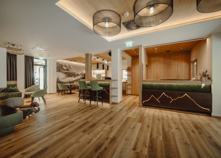 Modern hotel lobby with wooden floors, green seating, and a reception desk with mountain design.