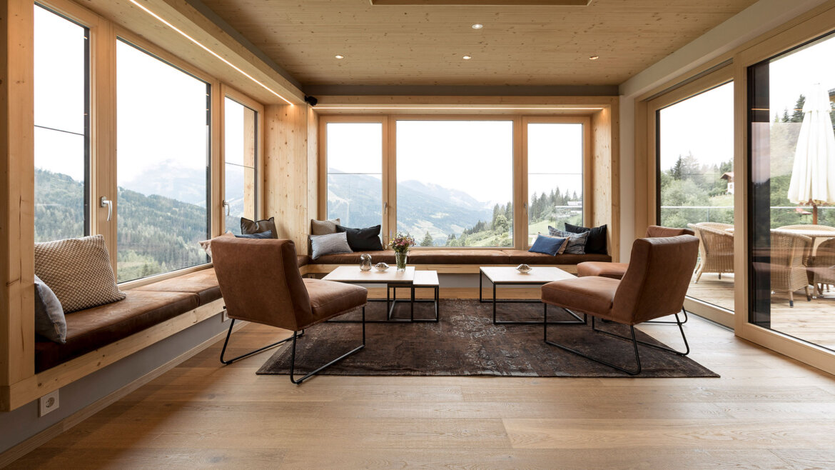 Modern living room with large windows, mountain views, and wooden accents at Naturhotel Edelweiss Wagrain. (Enlarged view)