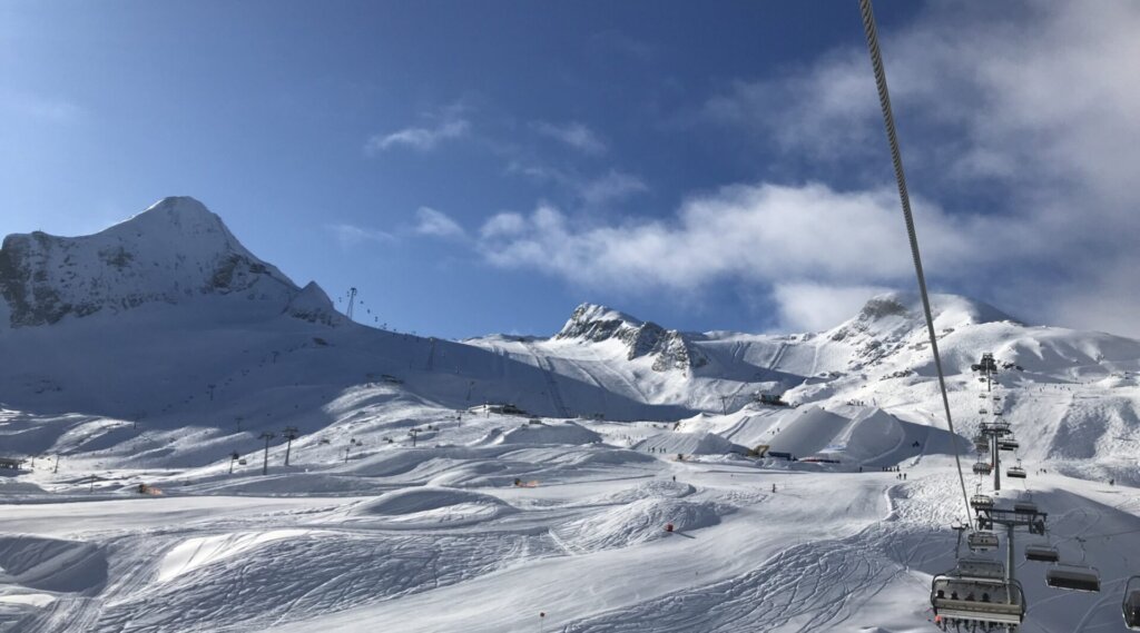 Skilift, der verschneite Berghänge unter einem strahlend blauen Himmel mit vereinzelten Wolken hinauffährt.