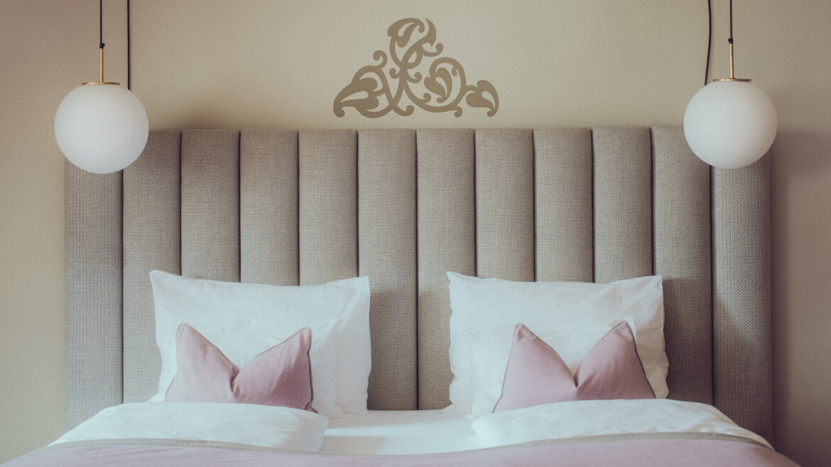 Elixhauser Wirt © Richard Schabetsberger Modern bed with grey tufted headboard, white and pink pillows, and two hanging round pendant lights. (Enlarged view)