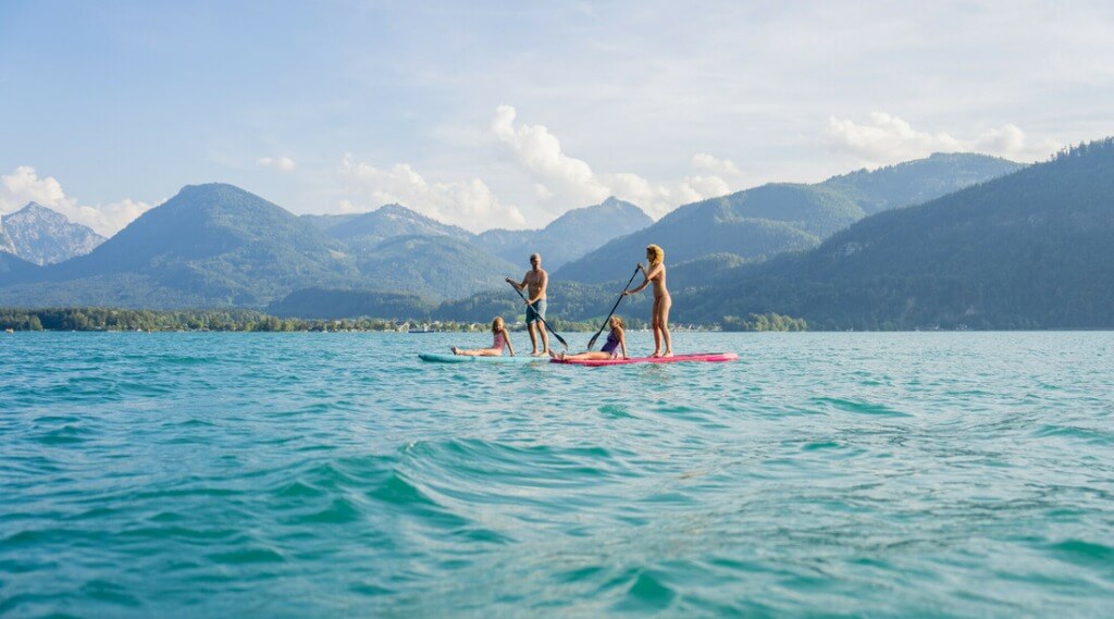 Water fun at Wolfgangsee © SalzburgerLand Tourismus, Christoph Oberschneider Four people paddleboarding on a lake with mountains and trees in the background under a partly cloudy sky. (Enlarged view)