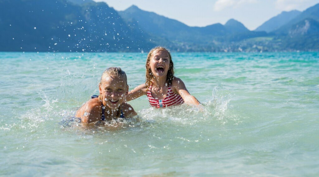 Swimming fun Wolfgangsee© SalzburgerLand Tourismus, Christoph Oberschneider, Two laughing children splashing in the crystal-clear waters of Wolfgangsee, with the mountains rising in the background on a sunny day. (Enlarged view)