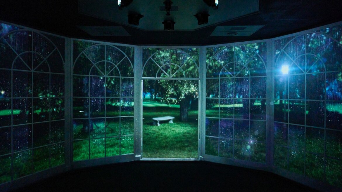 Part of the Sound of Music Museum the Gazebo A dark room with tall arched windows shows a nighttime garden scene with a stone bench and trees outside.