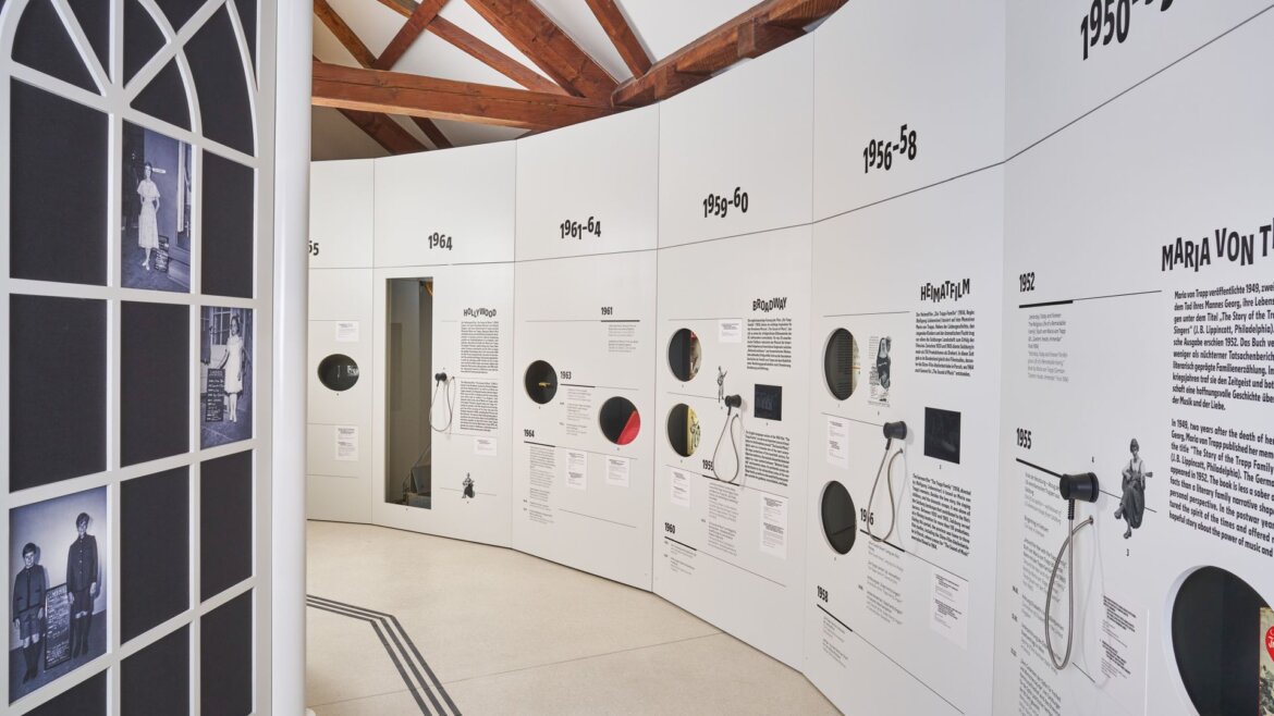 The Sound of Music Museum in Salzburg. White curved museum wall displays black-and-white photos and text, marking decades from 1950 to 1968.