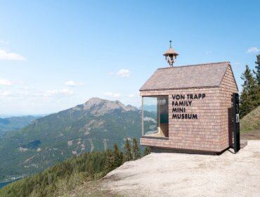 von Trapp Family Mini Museum (c) Zwölferhorn Seilbahn The von Trapp Family mini museum . A tiny shingled museum building on a mountain with “Von Trapp Family Mini Museum” sign, overlooking scenic hills.
