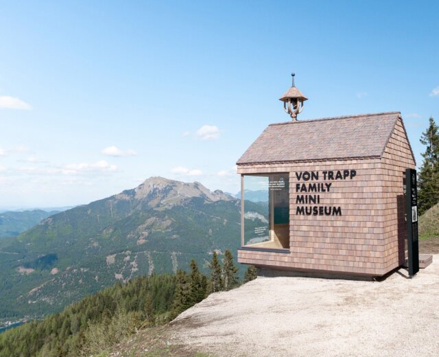 von Trapp Family Mini Museum (c) Zwölferhorn Seilbahn The von Trapp Family mini museum . A tiny shingled museum building on a mountain with “Von Trapp Family Mini Museum” sign, overlooking scenic hills.