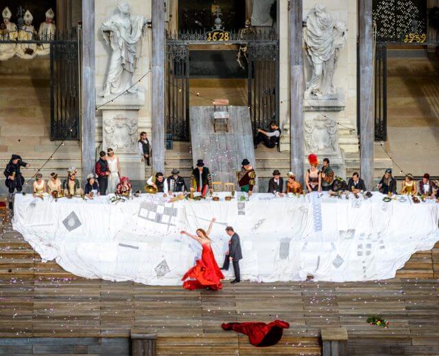 Jelmezes emberek vacsoráznak a nagy lépcsőkön, és ünneplik a kultúrát, miközben vörösbe öltözött táncosok mozognak a fehér ruhák alatt.