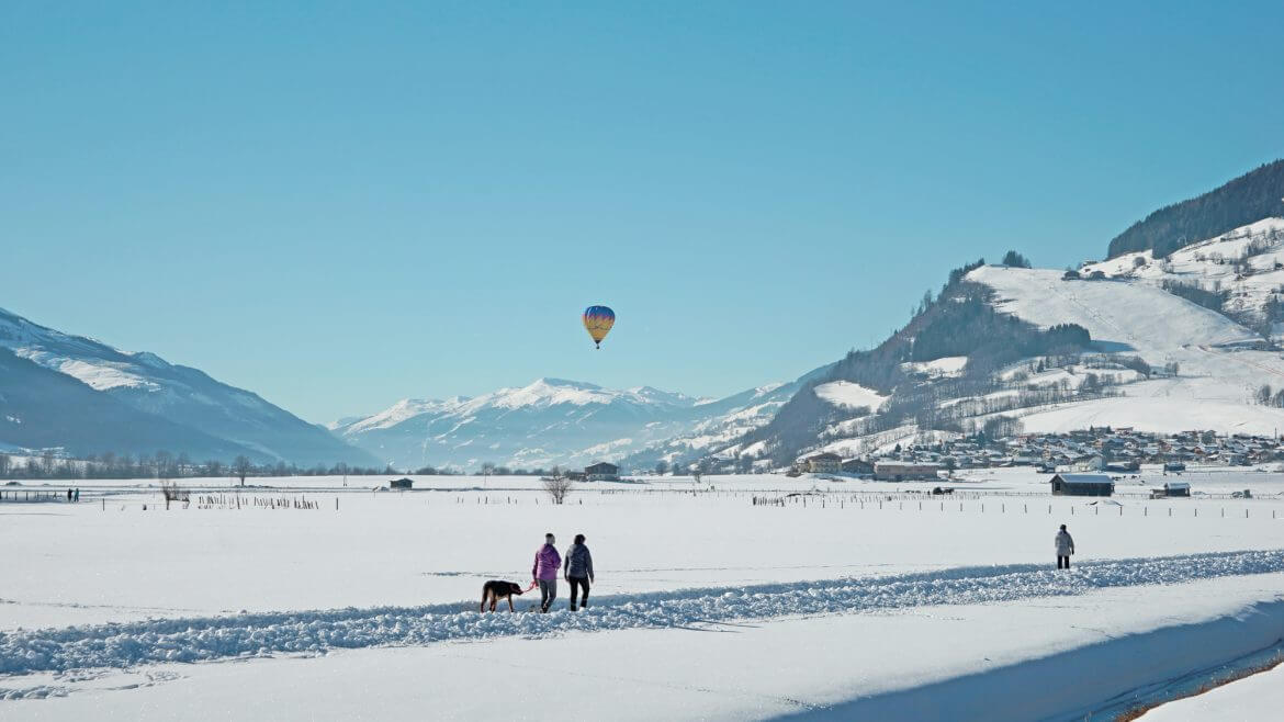 Nastrojowe chwile na Ziemi Salzburskiej: spacerowicze podziwiająkolorowe balony na niebie, a pasażerowie balonów zachwacyją się widokiem okolicy.