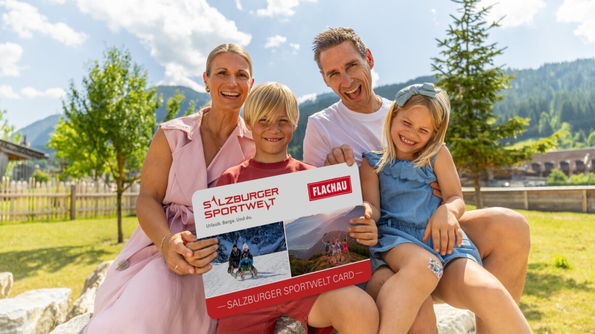 Egy mosolygós család ül a szabadban Flachauban, kezében egy nagy Salzburger Sportwelt kártyával egy napsütéses napon.
