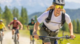 Kerékpárosok egy csoportja mountain bike-ozik egy napsütötte flachaui ösvényen, az előtérben egy mosolygó kerékpáros.