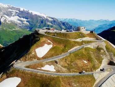 Kanyargós hegyi út autókkal és hófoltokkal a Hohe Tauern Nemzeti Parkban, tiszta kék ég alatt.