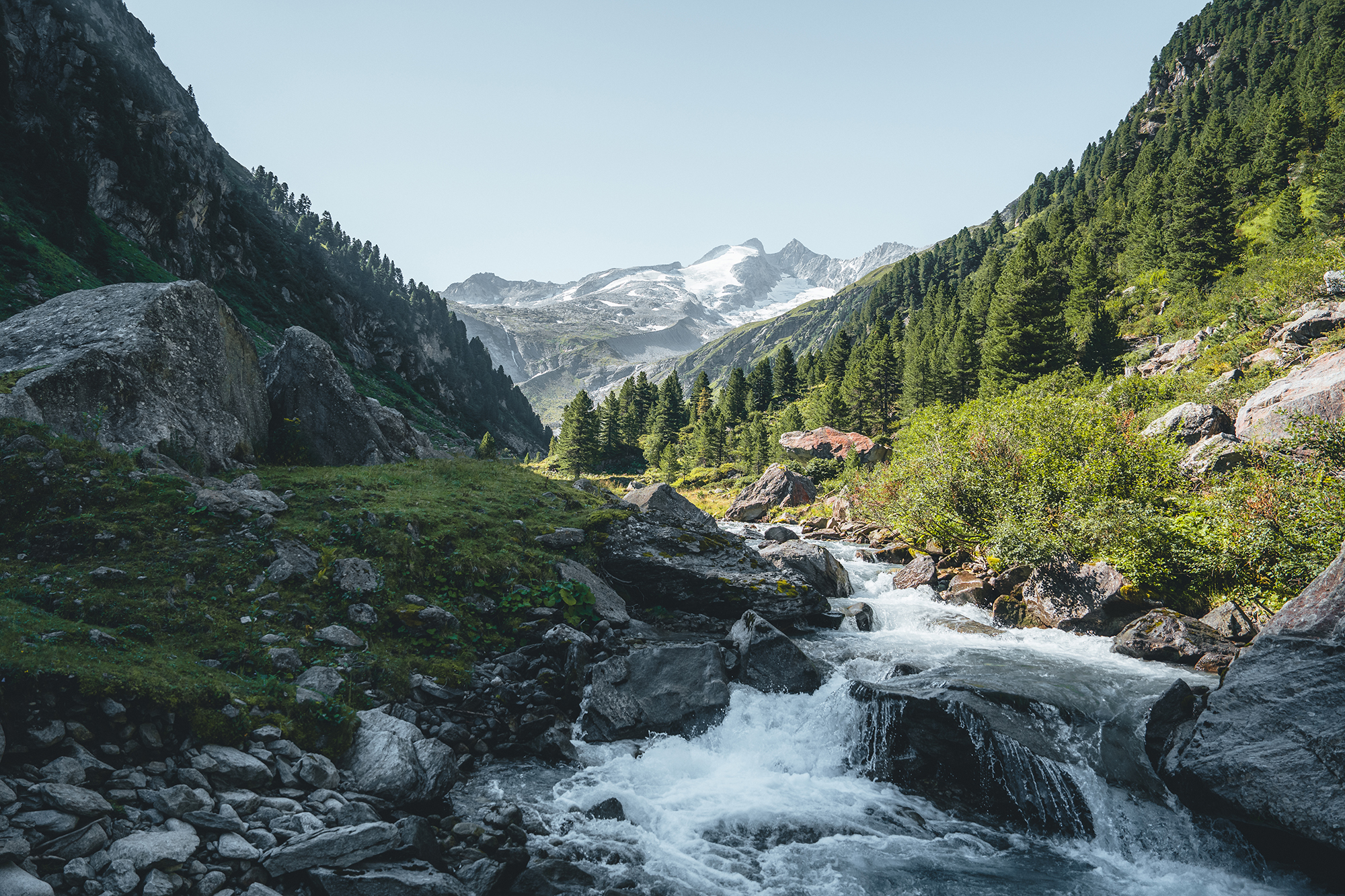 Egy hegyi patak folyik át a Hohe Tauern Nemzeti Park sziklás völgyén, egy gleccserrel borított csúcs felé.