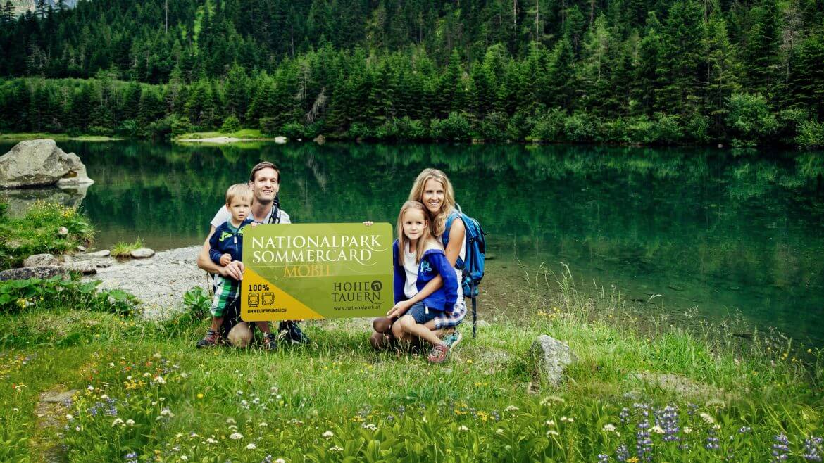 Egy család tartja a nagy méretű Magas-Tauern vendégkártyát a friss alpesi környezetben.