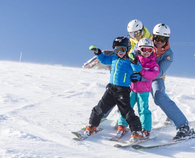 Egy négytagú család együtt síel a salzburgi Saalachtalban a tiszta kék ég alatt.