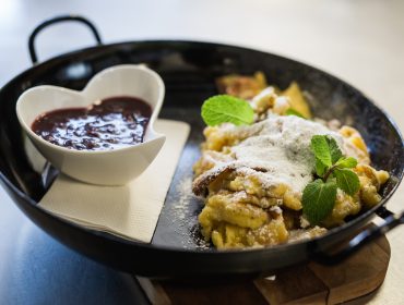 Egy serpenyő császármorzsa porcukorral meghintve, és egy szív alakú tál bogyós gyümölcsmártással, mentával díszítve.