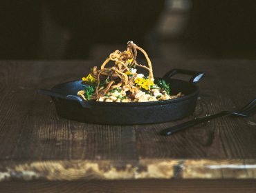 Egy öntöttvas serpenyőben sült hagymával és fűszernövényekkel megrakott ínyenc tál egy rusztikus faasztalon.