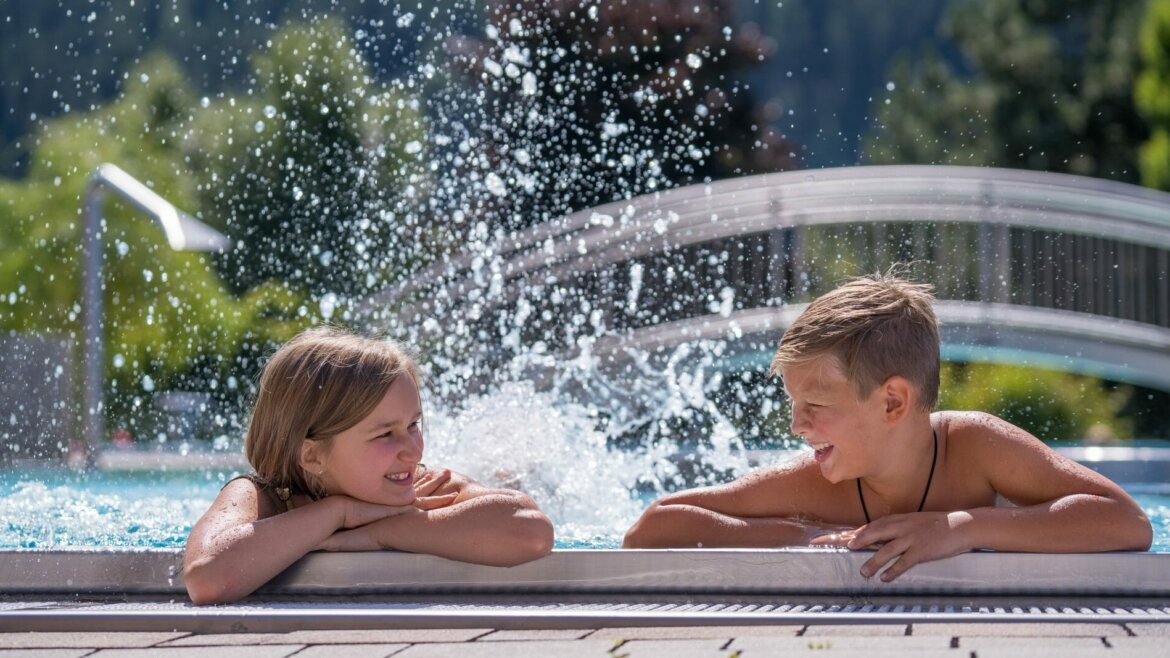 Két gyerek mosolyog egymásra egy medencében, vízzel fröcskölve, önmagam.lehetek. egy napsütéses napon. (Nagyított nézet)