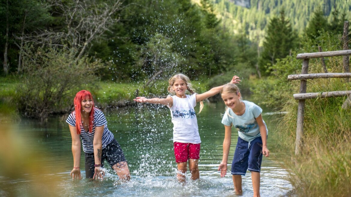 Három ember csobban egy patakban, zöldövezetben egy napsütéses napon a salzburgi Lungau-ban. (Nagyított nézet)
