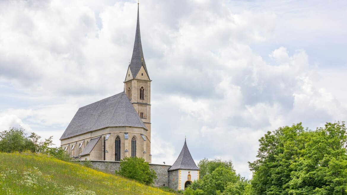 Történelmi templom magas toronnyal a salzburgi Lungau-ban, egy füves dombon, felhős ég alatt. (Nagyított nézet)