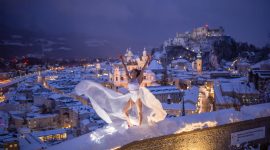 Salzburg téli látképe előtérben egy fehér ruhás táncosnővel.