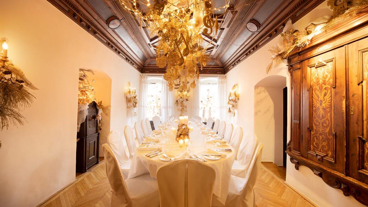 Fényűző terem, fehéren terített asztallal és aranydíszítéssel és függő csillárral.
