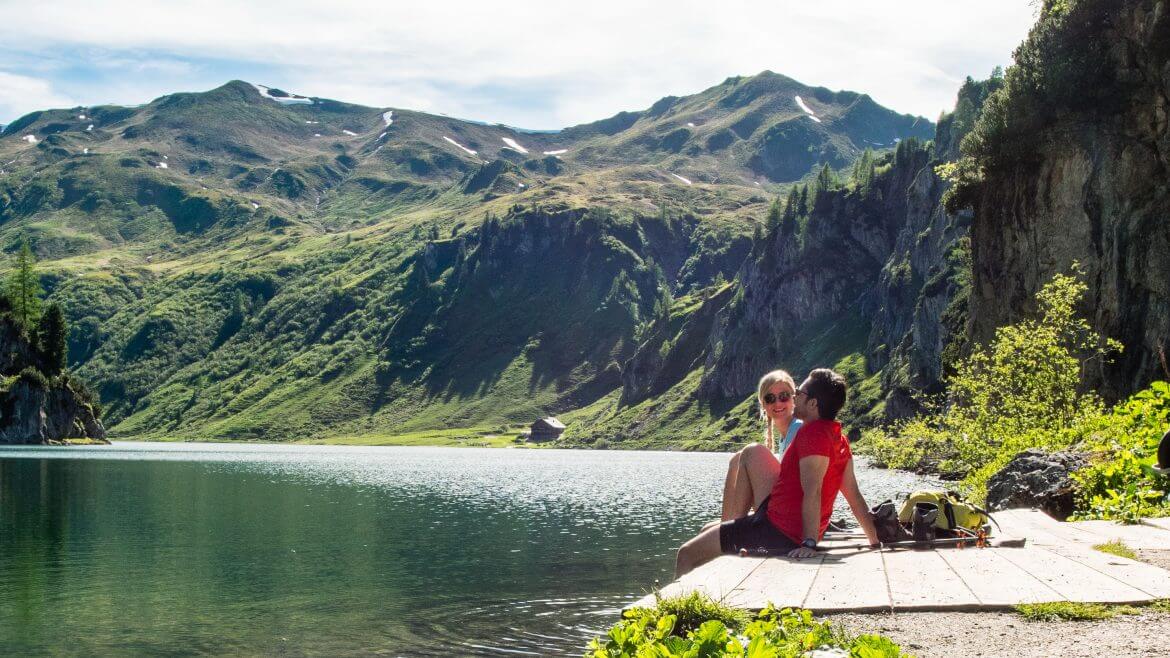 Pihenő kirándulók gyönyörködnek a hegyi panorámában a tiszta vizű Tapperkarsee tó partján