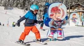 Játékos síélmények Egy gyermek síel el egy színes kabalafigurás tábla mellett az osztrák Dachstein West téli gyermekparkjában.