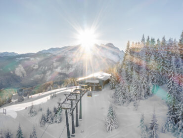 Napfelkelte a havas Dachstein West-hegység, sífelvonó állomás és hóval borított fenyőfák felett.