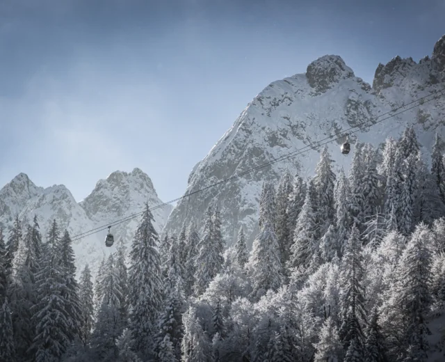 Télen a felvonók a hóval borított fák felett haladnak a Dachstein West szaggatott, hófedte hegyei felé.