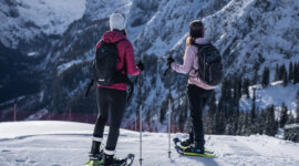 Két ember egy hótalpas túrán a Dachstein Westben, a havas hegyeket bámulják a tiszta égbolt alatt.