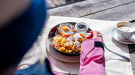 Regionális finomságok a hegyi hüttékben © JOsalzburg.com Egy rózsaszín kabátos ember osztrák Kaiserschmarrnt eszik gyümölcskompóttal és egy cappuccinóval St. Johannban, Salzburgban.