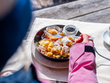 Regionális finomságok a hegyi hüttékben © JOsalzburg.com Egy rózsaszín kabátos ember osztrák Kaiserschmarrnt eszik gyümölcskompóttal és egy cappuccinóval St. Johannban, Salzburgban.