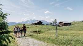 Négy ember sétál egy vidéki úton - zöld mezők, faházak, hegyek - egy családi üdülés St. Johann Salzburgban.