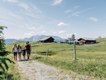 Négy ember sétál egy vidéki úton - zöld mezők, faházak, hegyek - egy családi üdülés St. Johann Salzburgban.