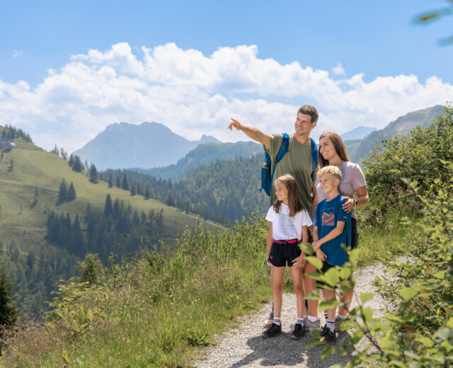 Négytagú család túrázás St. Johann Salzburgban, élvezve a festői zöld dombokat és a kék eget.