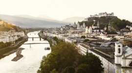 Salzburgon keresztül folyik a folyó a naplementében, kiemelve a salzburgi várat és a történelmi látványosságok Szent Johann Salzburgban.