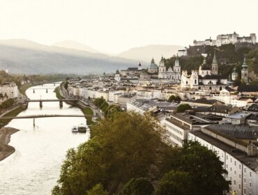 Salzburgon keresztül folyik a folyó a naplementében, kiemelve a salzburgi várat és a történelmi látványosságok Szent Johann Salzburgban.