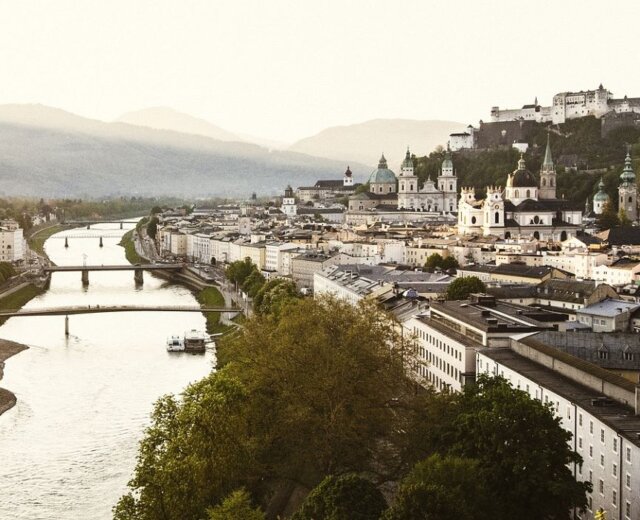 Salzburgon keresztül folyik a folyó a naplementében, kiemelve a salzburgi várat és a történelmi látványosságok Szent Johann Salzburgban.