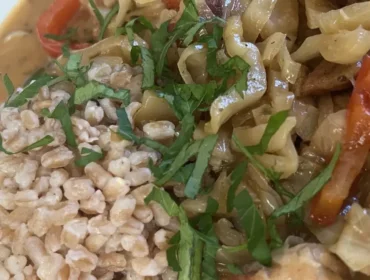 Egy tányér krémes Káposztás hús pörkölt zöldségekkel és fűszernövényekkel, egy adag barna rizzsel tálalva.