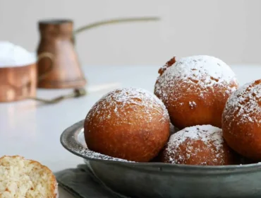 Fémtálban porcukorral porított túrós fánk, mellette egy felvágott egy szövetszalvétán.