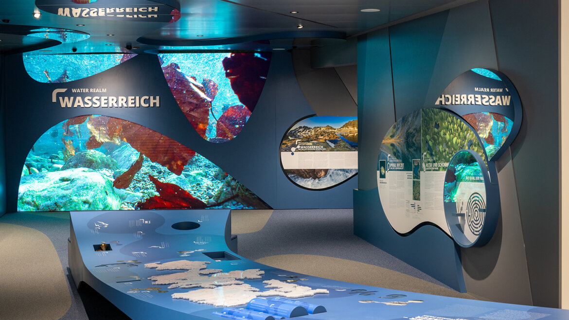 Megnyitó_NPZ_2024_05_07©Franz Reifmüller - Ferienregion Nationalpark Hohe Tauern Modern múzeumi kiállítás víz alatti témájú tárlókkal, kék falakkal és interaktív információs táblákkal. (Nagyított nézet)