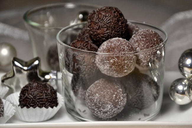 Csokoládé trüffelekkel töltött pohár, némelyiket szórócukorral, másokat cukorral bevonva, ezüst díszek mellett.