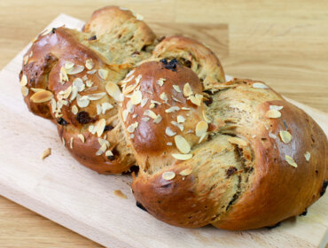 Fruehstuecksstriezel-fuer-Weihnachten-scaled Egy fából készült vágódeszkán szeletelt mandulával megrakott, fonott édes kenyér.